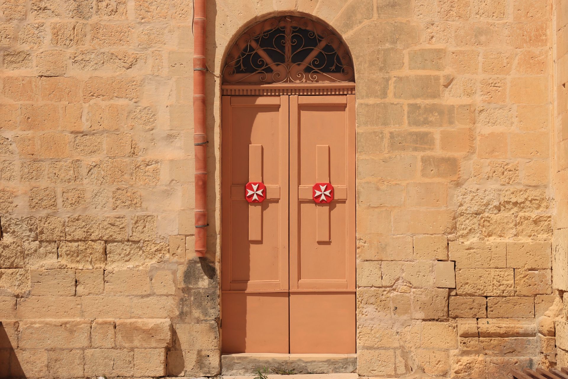Charming door with Maltese cross on a historic stone building in Valletta, Malta.